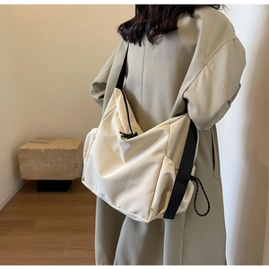 Detail of off-white canvas hobo bag featuring black straps and adjustable drawstring side