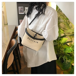 Détail du sac seau en paille tressée avec logo RESTAIN et style bandoulière noire chic