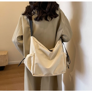 Detail view of a beige canvas crossbody bag with black strap and side drawstring details
