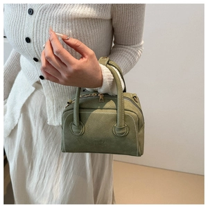 Macro view of green faux leather handbag featuring white stitching and double zippers
