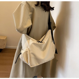 Detail of minimalist beige canvas shoulder bag featuring woven zipper pull and wide strap