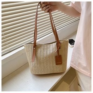 Close-up of beige woven straw tote bag featuring brown leather straps and detail