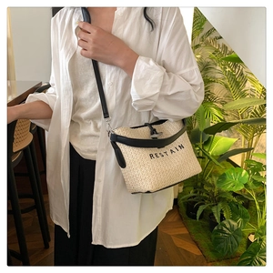 Gros plan sur un sac bandoulière tissé beige avec finitions en cuir noir et broderie