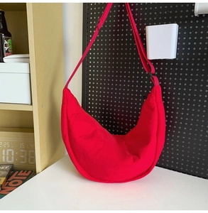 Detail view of a red quilted half-moon crossbody bag on a white table in an urban setting