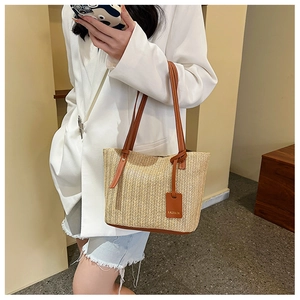Detail of a woven straw tote bag with brown leather handles worn by a model in a blazer