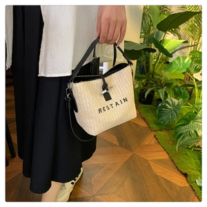 Close-up of woven straw bucket bag with black leather handle and RESTAIN embroidery
