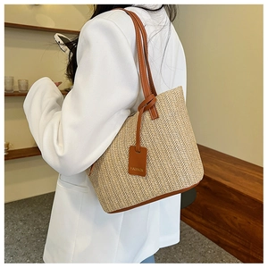 Close-up of woven straw tote bag featuring brown leather straps and fashion tag details