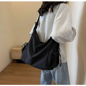 Detail of a large black canvas crossbody bag with drawstring side pocket and wide strap