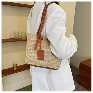 Detail of woven straw tote bag with brown leather straps shown on a shoulder