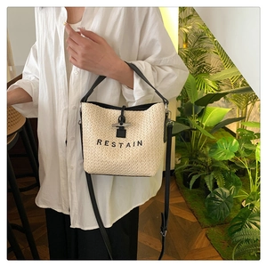 Detail of woven straw bucket bag featuring RESTAIN embroidery and black leather strap