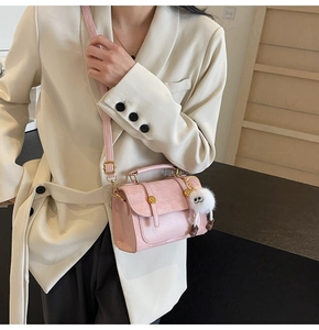 Close-up of pink PU leather crossbody bag with metal handle and cute white plush charm