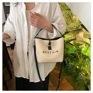 Détail du sac seau en paille tressée avec bordure en cuir noir, bouton corne et logo RESTAIN