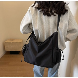 Detail view of a large black nylon crossbody bag with drawstring side pockets and adjustable strap