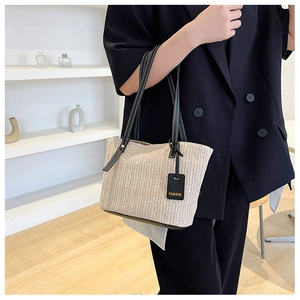 Detail of woven straw tote bag featuring black leather handles and white contrast stitching
