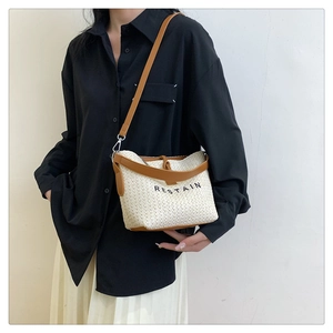 Detail view of woven straw crossbody bag with leather trim and Restain logo on a model
