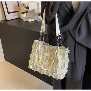 Detail der hellgrünen Tweed-Tasche mit Fransen, Lederriemen und silbernen Kettenelementen