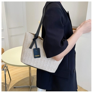 Detail shot of the woven straw tote bag with black strap and FASHION leather tag