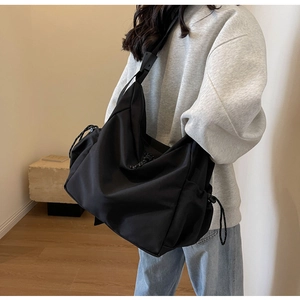 Detail of a large black waterproof crossbody bag with drawstring side and wide shoulder strap