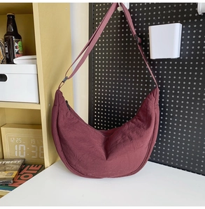Close-up of a burgundy crescent nylon crossbody bag hanging on a display hook