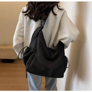 Detail view of the wide adjustable strap and side drawstring on black canvas crossbody bag