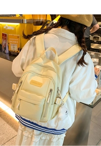 Detail of a creamy yellow nylon backpack showing front pockets and fluffy pompom charm