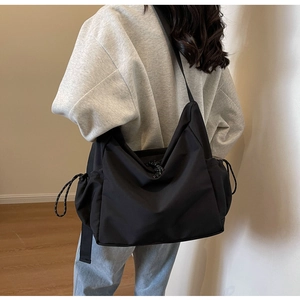 Detail of black crossbody bag with adjustable wide shoulder strap and drawstring side pockets