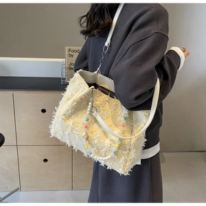 Detailansicht der gelben Tweed-Tasche mit Fransen und bunter Perlenkette am Schultergurt