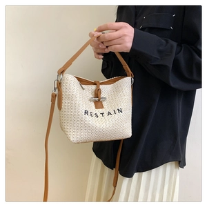 Detail of woven straw bucket bag with Restain embroidery and brown leather handle