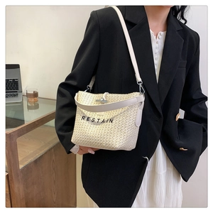 Détail du sac seau en paille tissée avec logo RESTAIN et bandoulière en cuir crème