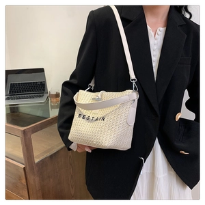 Close-up of beige woven straw bucket bag with Restain embroidery and white leather strap