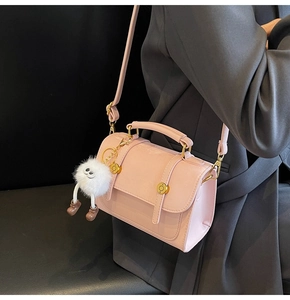 Detail shot of a pink PU leather handbag with a cute white plush monster charm
