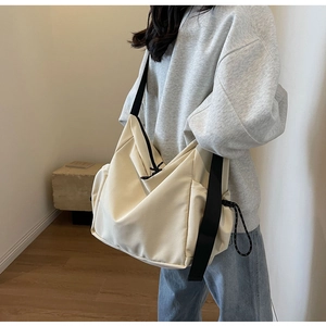Detail of a beige canvas crossbody hobo bag with a black strap worn by a model