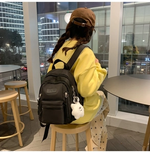 Close-up of black PU leather mini backpack with a white plush cloud charm and logo detail