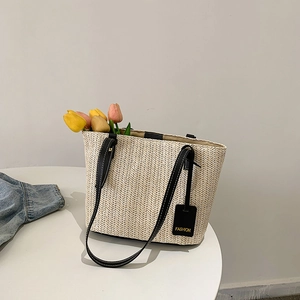 Minimalist straw tote bag with black leather handles and fresh tulips in spring setting