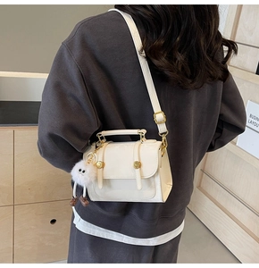 Detail view of cream glossy PU leather handbag with gold hardware and fuzzy monster charm