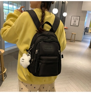 Detail view of black waterproof backpack featuring multi-layer zippers and plush bear charm