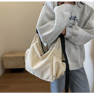 Detail view of large cream tote bag featuring side drawstring pocket and black wide strap