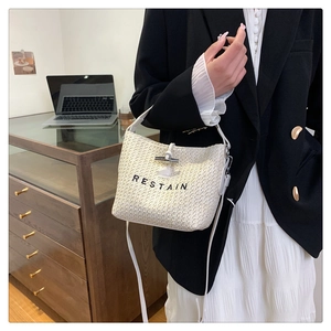 Detail of white woven bucket bag featuring RESTAIN embroidery and bamboo buckle