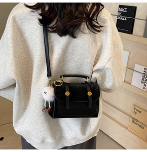 Detail of black matte PU leather bag with flap cover and white plush monster charm accessory