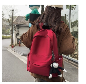 Outdoor shot of a red nylon backpack featuring multiple pockets and a cute plush monkey charm