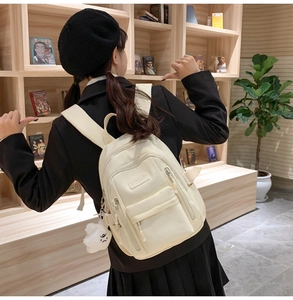 Detailed view of the creamy white backpack with a plush cloud charm on a model in a library