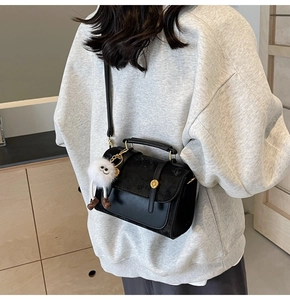 Side view of a vintage black crossbody bag with a white plush doll charm and metal buckle