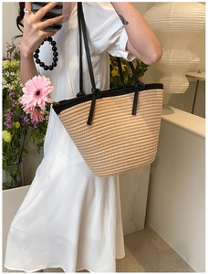 Détail d'un sac cabas en paille tressée avec anses noires et texture beige chic