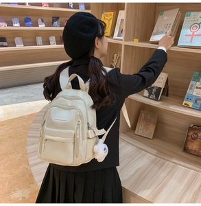 Detailed view of stylish cream white backpack with plush charm in a bookstore setting