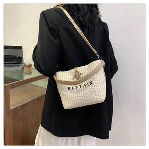Close-up of beige woven bucket bag with leather trim and Restain embroidery detail