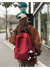 Detail of red nylon backpack featuring a black monkey plush keychain in an outdoor street setting