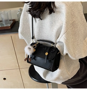 Detail of black PU crossbody bag featuring golden magnetic snaps and white plush toy charm