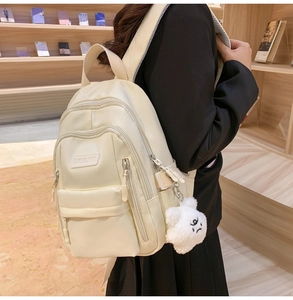 Close-up of cream white nylon backpack with multiple zippers and a plush cloud charm