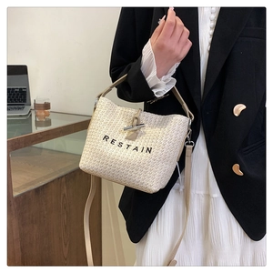 Détail du sac seau tissé beige avec fermeture à bascule et texte brodé sur le devant