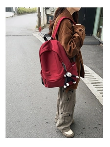 Outdoor shot of a burgundy nylon backpack with a decorative monkey keychain charm